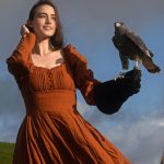 a woman in an orange dress holding a bird on her arm